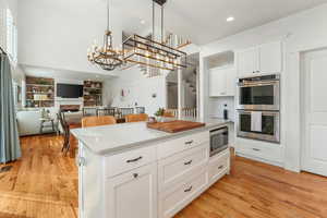 Kitchen featuring stainless steel appliances, white cabinets, open floor plan, hanging light fixtures, and light countertops