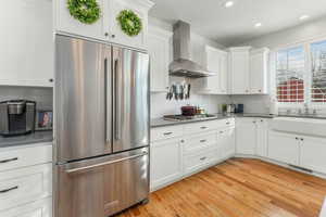 Kitchen featuring light wood-style flooring, a sink, white cabinets, appliances with stainless steel finishes, and wall chimney exhaust hood