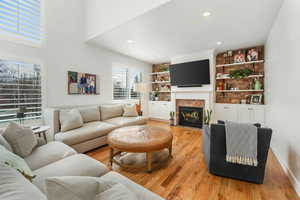 Living room with built in features, light wood finished floors, recessed lighting, a fireplace with flush hearth, and baseboards