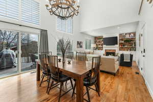 Dining area featuring a warm lit fireplace, visible vents, light wood-style flooring, a high ceiling, and a chandelier