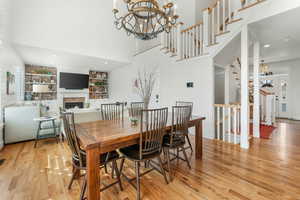 Dining area with a notable chandelier, a fireplace, built in features, stairs, and light wood finished floors