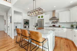 Kitchen with white cabinets, wall chimney range hood, stainless steel appliances, and a center island