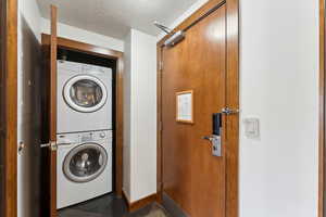 Clothes washing area with stacked washer / drying machine, tile patterned floors, and baseboards