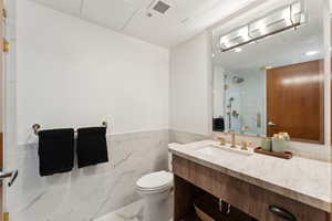 Bathroom with a shower, toilet, vanity, tile walls, and wainscoting