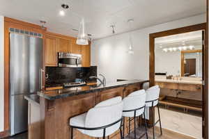 Kitchen featuring stainless steel appliances, decorative backsplash, a breakfast bar, pendant lighting, and dark stone countertops