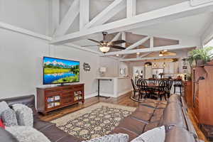 Living room featuring baseboards, a ceiling fan, wood finished floors, high vaulted ceiling, and beam ceiling