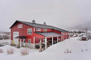 Snow covered rear of property with an outbuilding, a detached garage, metal roof, a mountain view, and a barn