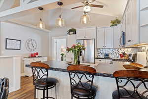 Kitchen with a breakfast bar area, stainless steel appliances, wood finished floors, white cabinetry, and dark countertops