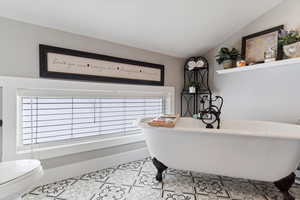 Full bath with baseboards, toilet, a soaking tub, tile patterned flooring, and vaulted ceiling