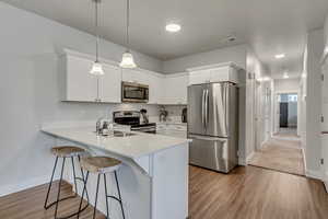 Kitchen featuring pendant lighting, stainless steel appliances, light countertops, white cabinetry, and a peninsula