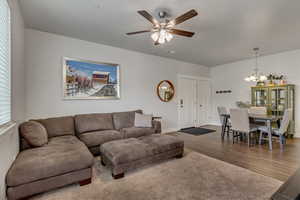 Living area with ceiling fan with notable chandelier, visible vents, baseboards, and wood finished floors