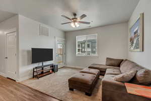 Living room featuring light wood finished floors, visible vents, baseboards, ceiling fan, and a textured ceiling