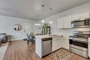 Kitchen featuring a peninsula, a sink, white cabinetry, hanging light fixtures, and appliances with stainless steel finishes