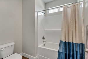 Full bathroom with shower / bath combo with shower curtain, toilet, and baseboards