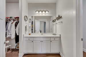 Bathroom with a walk in closet, vanity, baseboards, and wood finished floors