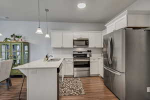 Kitchen featuring decorative light fixtures, light countertops, appliances with stainless steel finishes, a peninsula, and a kitchen breakfast bar