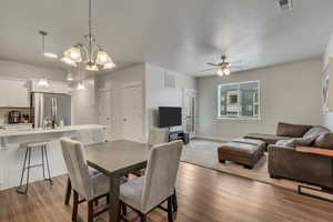 Dining area with ceiling fan with notable chandelier, visible vents, baseboards, and wood finished floors