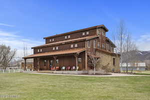 Rear view of property featuring a yard, stone siding, fence, and a mountain view