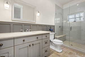 Full bath featuring toilet, a decorative wall, vanity, wainscoting, and a stall shower