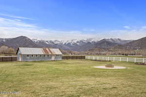 View of yard with an outdoor fire pit, a rural view, fence, an outdoor structure, and a mountain view