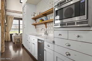 Kitchen featuring white cabinets, backsplash, stainless steel appliances, open shelves, and a sink