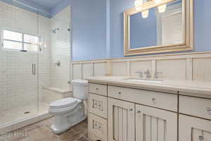 Full bath with a stall shower, wainscoting, vanity, and toilet