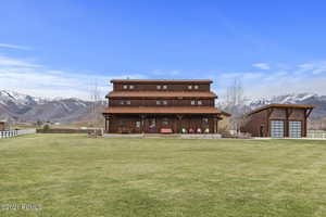 Rear view of property featuring fence, a mountain view, and a lawn