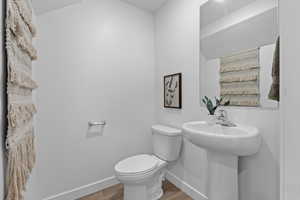 Half bathroom with wood finished floors, toilet, and baseboards