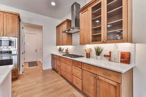 Kitchen featuring light hardwood / wood-style flooring, backsplash, wall chimney range hood, stainless steel appliances, and light stone countertops