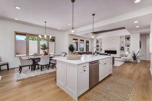 Kitchen featuring a center island with sink, light wood-type flooring, white cabinetry, decorative light fixtures, and stainless steel dishwasher