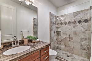 Bathroom with a notable chandelier, toilet, vanity, and walk in shower