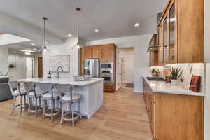 Kitchen with a kitchen island with sink, stainless steel appliances, light hardwood / wood-style floors, sink, and pendant lighting