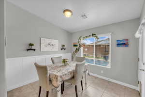 Dining area with a wainscoted wall, visible vents, a decorative wall, and light tile patterned flooring