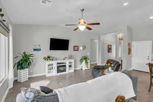 Living room with visible vents, a glass covered fireplace, tile patterned flooring, vaulted ceiling, and ceiling fan with notable chandelier