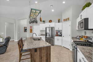 Kitchen featuring a center island with sink, appliances with stainless steel finishes, a sink, light stone countertops, and a kitchen breakfast bar