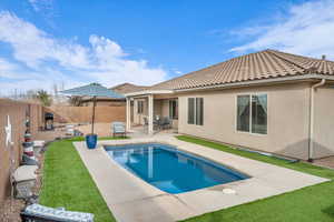 Rear view of property with stucco siding, a fenced backyard, a fenced in pool, and a tiled roof