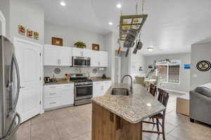 Kitchen with a center island with sink, white cabinets, appliances with stainless steel finishes, light stone countertops, and a sink