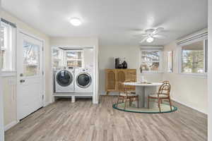 Laundry room featuring light wood finished floors, a textured ceiling, separate washer and dryer, laundry area, and baseboards