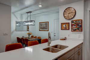 Kitchen with silestone countertops, a sink, hanging light fixtures, and a textured ceiling