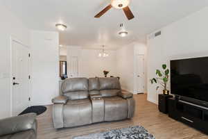 Living room featuring ceiling fan with notable chandelier and light wood-type flooring