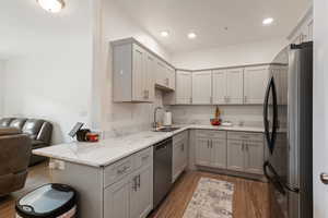 Kitchen featuring kitchen peninsula, gray cabinetry, sink, dishwasher, and black fridge