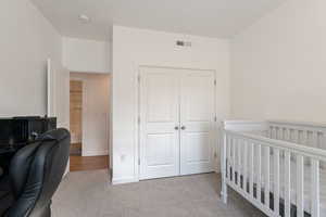 Bedroom with light carpet, a closet, and a nursery area