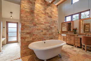 Full bathroom featuring a freestanding tub, stone tile floors, a sink, a towering ceiling, and double vanity