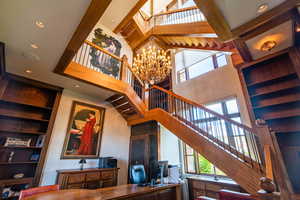 Living area with built in features, beam ceiling, a chandelier, and a high ceiling