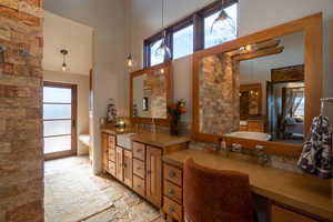 Full bath featuring a towering ceiling, vanity, a wealth of natural light, and stone tile floors