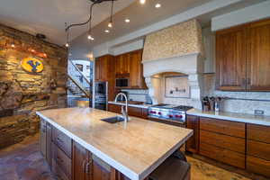 Kitchen featuring a kitchen island with sink, stainless steel appliances, a sink, tasteful backsplash, and stone tile flooring