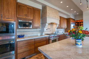 Kitchen with light countertops, appliances with stainless steel finishes, custom exhaust hood, decorative backsplash, and a warming drawer