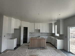 Kitchen with white cabinets, baseboards, a center island, and a textured ceiling