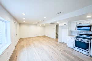 Kitchen with light countertops, visible vents, appliances with stainless steel finishes, white cabinets, and light wood-type flooring