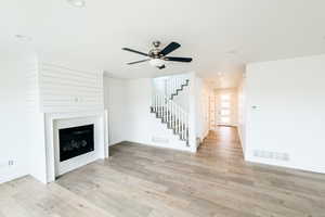 Unfurnished living room with light wood-style flooring, stairway, a glass covered fireplace, and visible vents